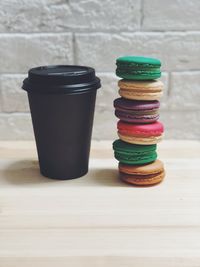 Colorful stacked macaroons by disposable cup on table