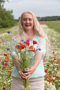 Beautiful middle-aged blonde woman stands among a flowering field of poppies