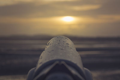 Close-up of wet coin-operated binoculars against sky during sunset