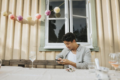 Young man using smart phone while sitting at table during dinner party