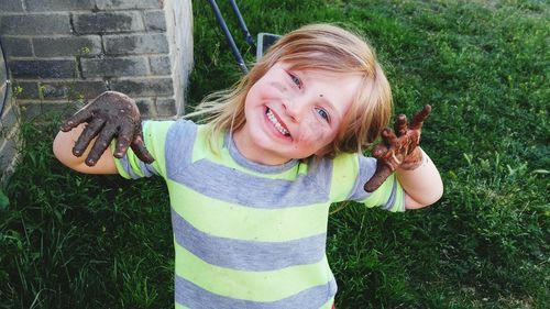 High angle portrait of cute smiling girl with muddy hand standing on grass