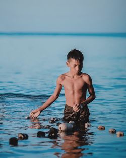 Shirtless man fishing in sea against sky