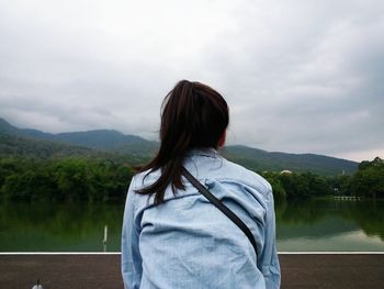 Rear view of woman standing by lake against sky