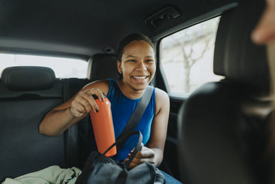 Happy teenage girl with water bottle sitting in car