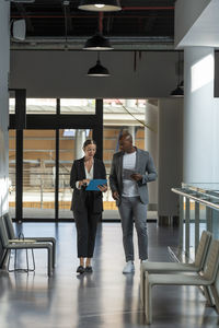 Business colleagues walking and discussing over clipboard in office corridor