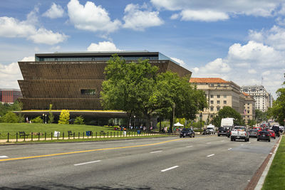 Road by buildings in city against sky