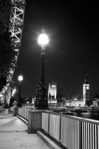 Illuminated street light by building against sky at night