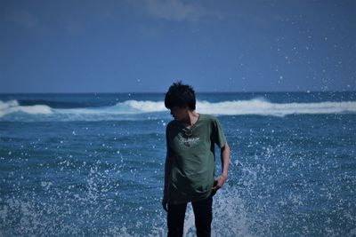 Young man is standing on the beach and there are waves behind him