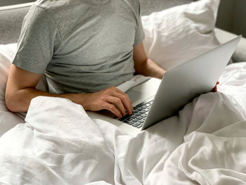 Middle aged adult man using laptop at home in bed vibes white bedsheets alone early morning working