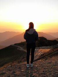 Rear view of man standing on mountain during sunset