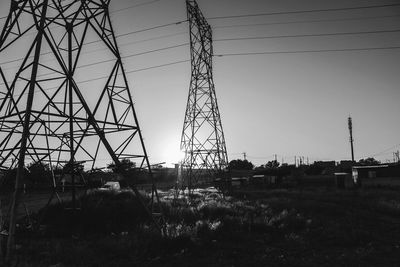 Silhouette electricity pylon on field against clear sky