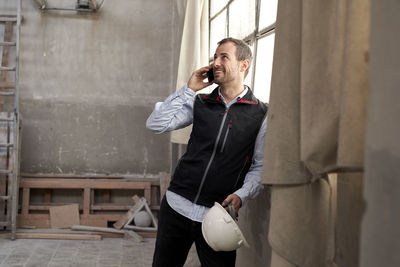 Smiling male contractor talking over smart phone while standing in building