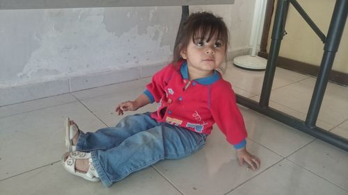 Cute girl looking down while sitting on tiled floor