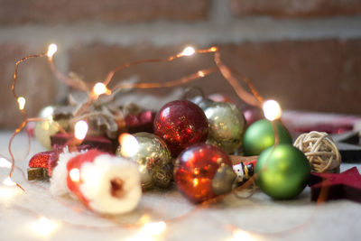 Close-up of christmas decoration christmas lights and christmas ornaments on table against brick wal