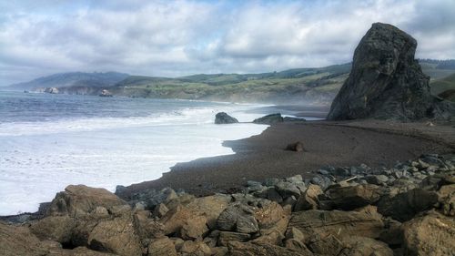 Scenic view of rocks on ocean coastline and beach against sky