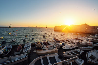 Boats moored at beach against sky during sunset