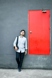 Young man looking away while standing against wall