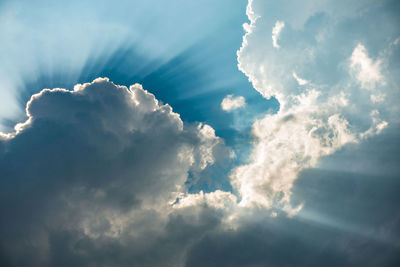 Low angle view of sunlight streaming through clouds