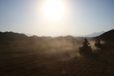 People riding motorcycle on field against sky during sunset