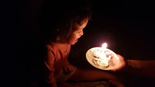 Close-up of hand holding illuminated candle in plate by crying girl in dark