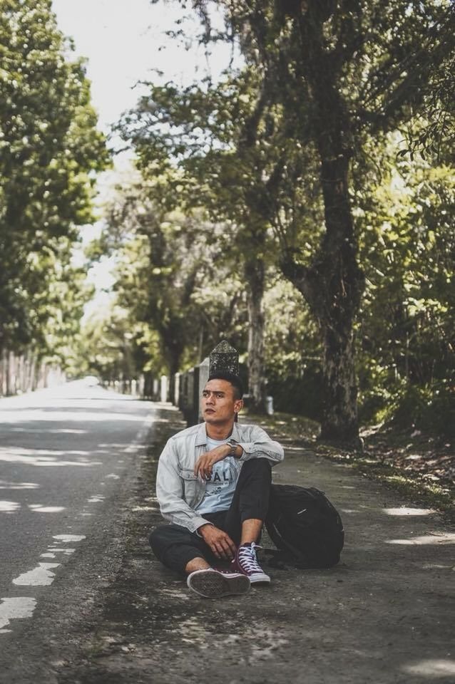 PORTRAIT OF MAN SITTING ON ROAD AGAINST TREES