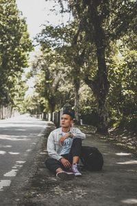 Portrait of young man sitting on road against trees