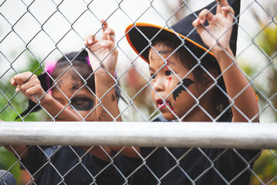Close-up of friends wearing halloween costumes looking through chainlink fence