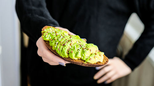 Female hand holding healthy avocado toast. ripe hass avocado, wholegrain bread, sesame flax seeds. 