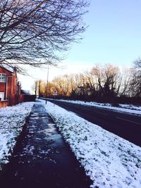 Snow covered road amidst bare trees against clear sky