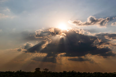 Low angle view of sunlight streaming through clouds during sunset