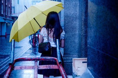 Rear view of woman with yellow umbrella in city during monsoon