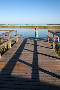 Shadow of railing on pier against clear sky