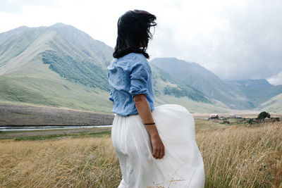 Rear view of woman standing on field against mountains