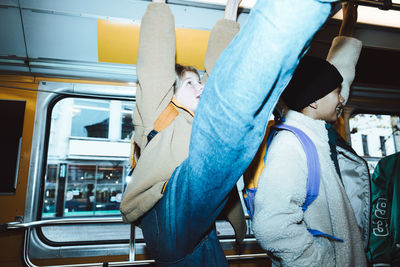 Girl with leg up standing by male friends traveling in tram