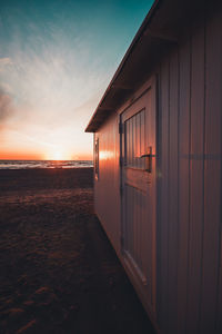 Beach hut by sea against sky during sunset