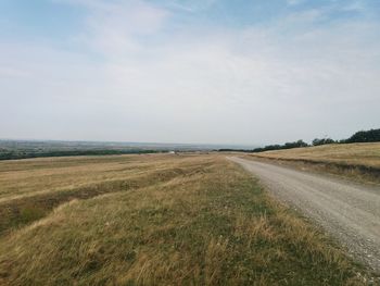 Scenic view of road amidst field against sky