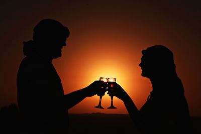 Silhouette couple toasting against orange sky