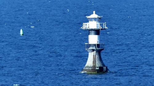 Lighthouse by sea against blue sky