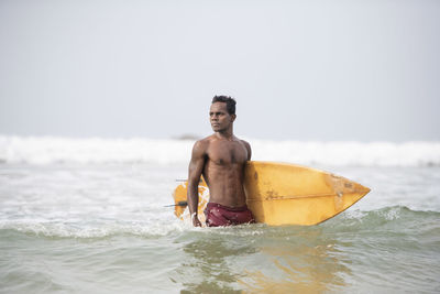 Full length of shirtless man in sea against sky