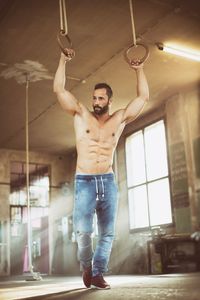 Full length of shirtless muscular man holding gymnastic rings 