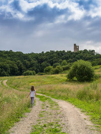 Rear view of woman walking by plants against sky