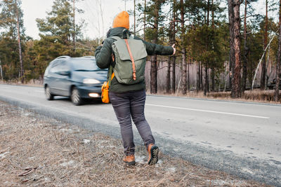 Middle-aged active woman with backpack hiking in road and gesture trying to stop car, winter travel