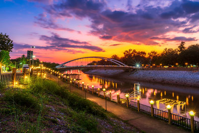 Illuminated bridge over river at sunset