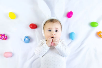 High angle view of baby girl with easter egg toy lying on bed at home