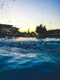 Wet glass window against sky during sunset