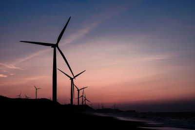 Silhouette wind turbines on land against sky during sunset