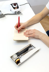 Unrecognizable nail master makes notes in notebook with pen, sitting at workstation, table in nail