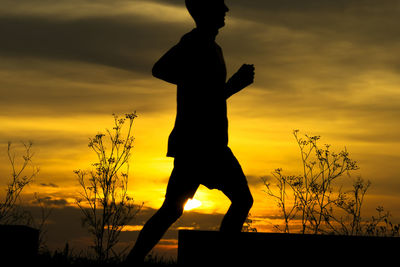 Silhouette of man jogging against orange sky