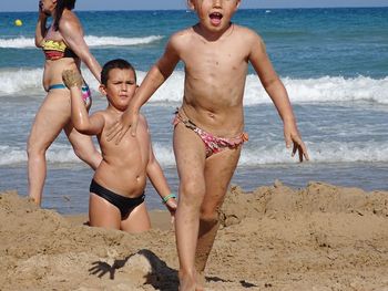 Shirtless siblings playing with sand at beach