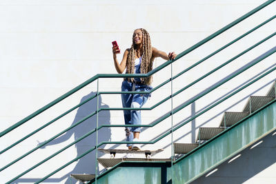 Full length of woman using mobile phone standing on staircase